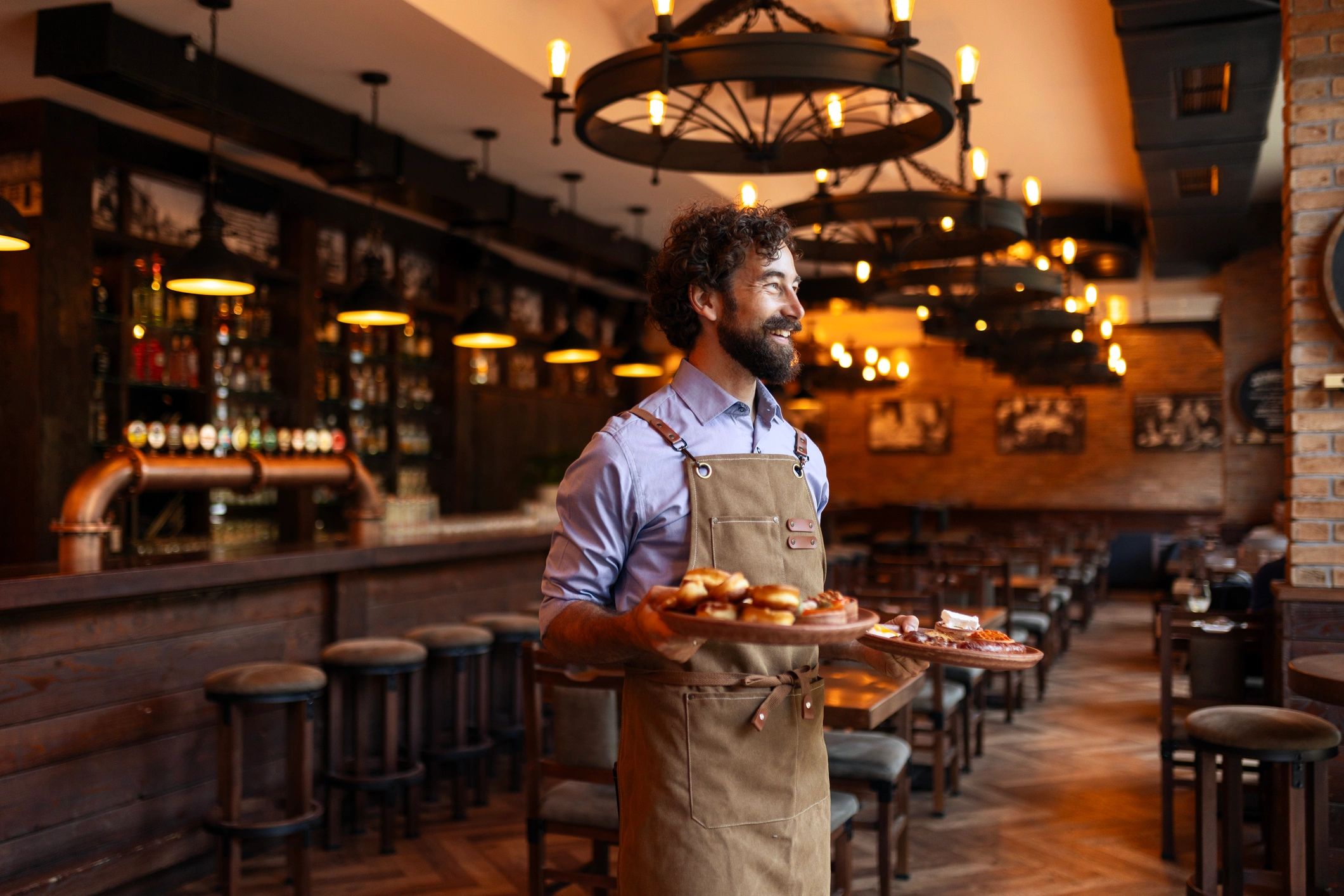 Smiling waiter serving plates of food in a bar setting